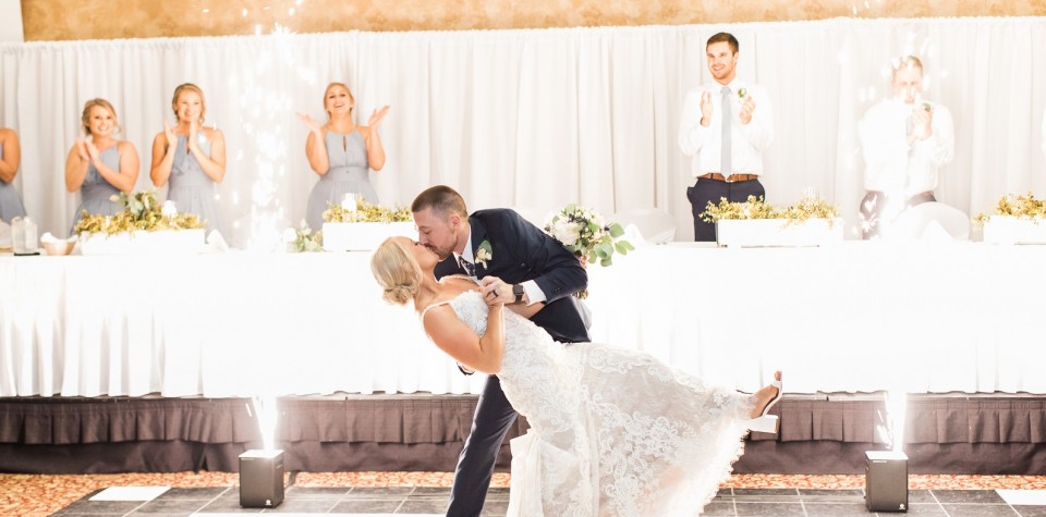 Groom dipping bride and kissing her while bridal party claps and cheers